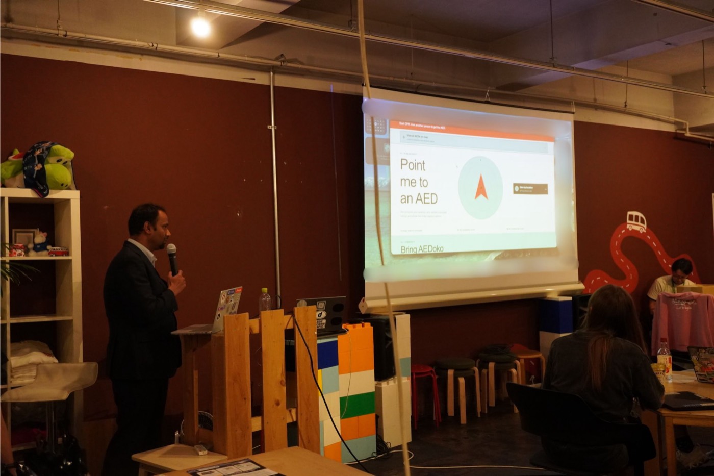 Presenter showing the AEDoko app on screen — Point me to an AED